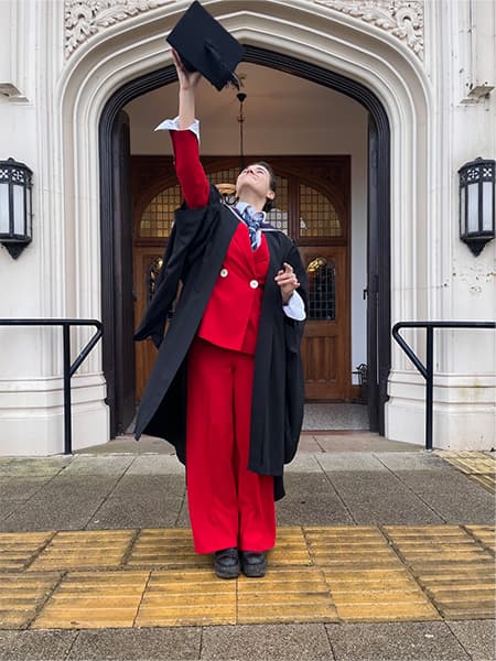 Mona wearing graduation gown and mortarboard outside Hazlerigg Building.