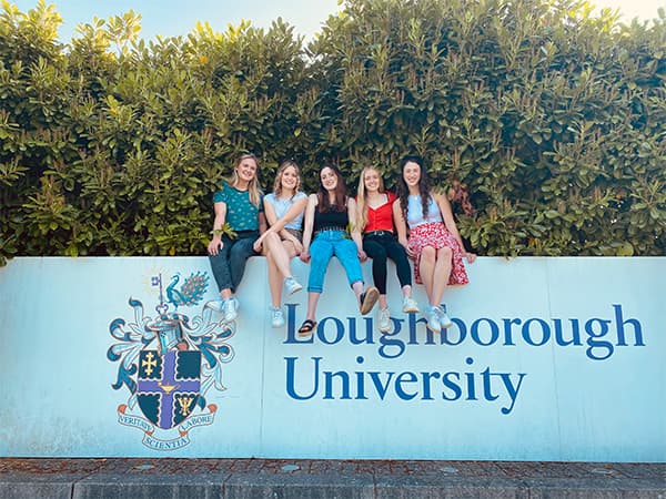 Olivia and a group of friends sitting on the Loughborough University sign on campus.
