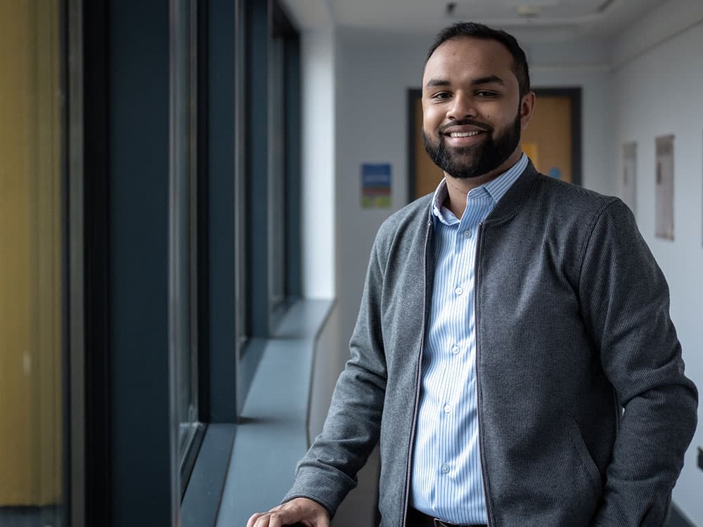 A student standing in a corridor smiling towards camera.