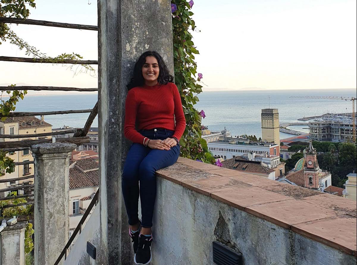 Shannon sitting on a wall with the background of the sea in Italy. 