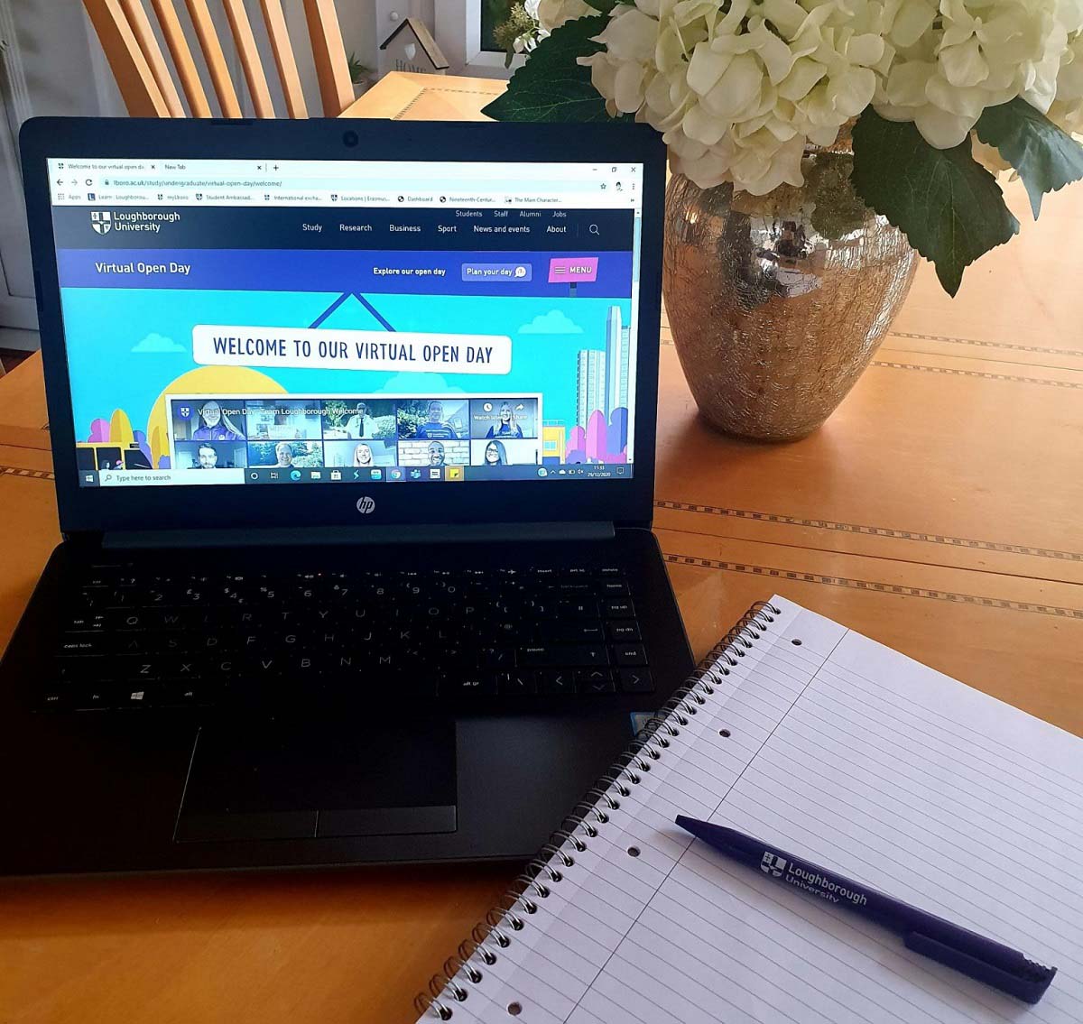 A Laptop with Loughborough University's virtual open day open on it, with a pen and notepad by the side of the laptop. 