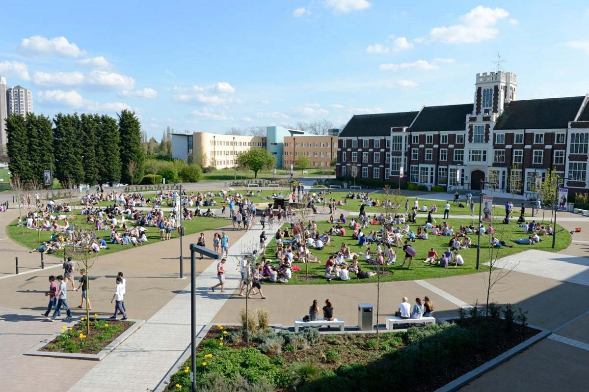 Overhead image of the Loughborough University fountain and lawns in front of the hazlerigg and rutland buildings. Groups of people are sitting on the lawns surrounding the fountain. 