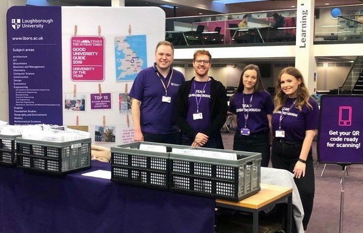 Mia standing in front of a Loughborough University banner with three colleagues during her placement year. 