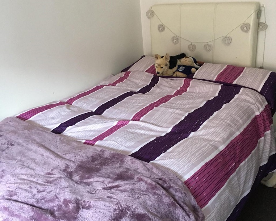 A photo of Emma's bed. Which has purple and pink stripy bedding. 