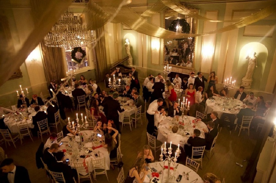 An overhead image of students sitting at tables at a university hall ball event.