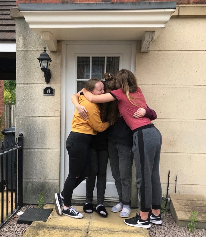 Caroline and three housemates hugging outside their house.  