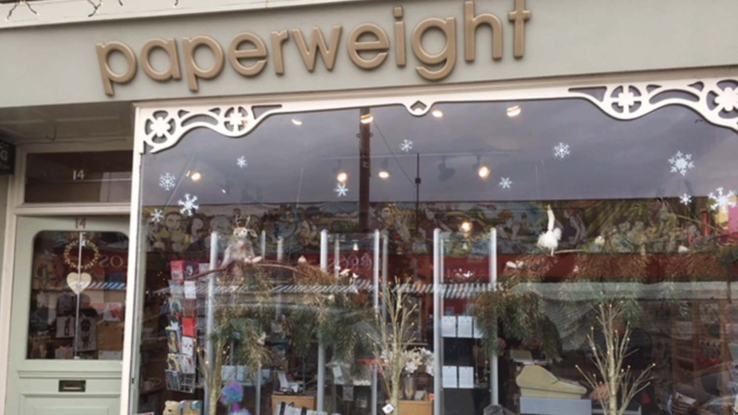 The shop front of Paperweight, a local shop in Loughborough town centre. It has a glass window at the front and a gold banner with the name 'Paperweight' above the shop. 