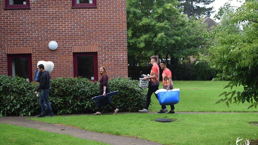 Two fresher helpers helping a first year carry their stuff into their student accommodation. 