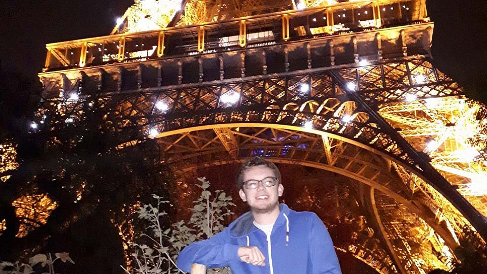 Joe in front of the Eiffel Tower at night when it is lit up.