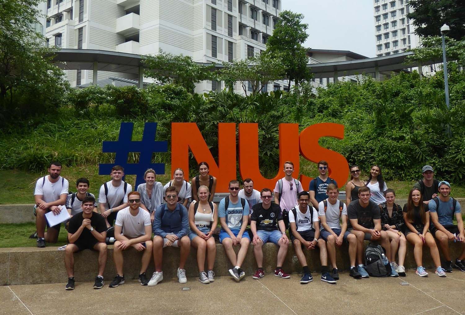 Joe and other students during a field trip sitting in front of a #NUS sign. 