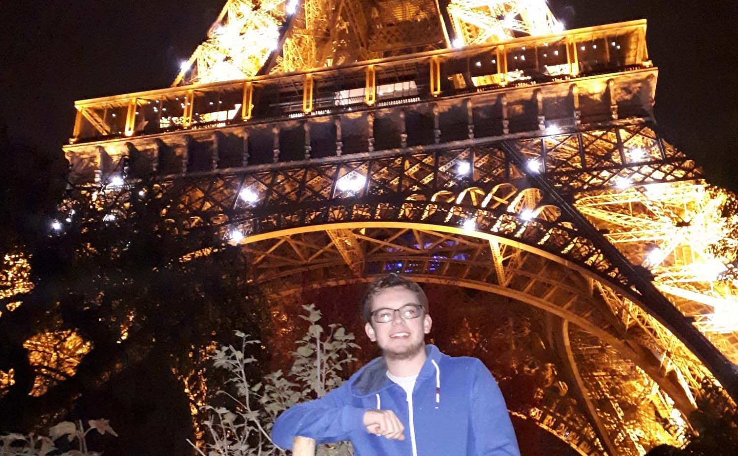 Joe in front of the Eiffel Tower at night when it is lit up. 