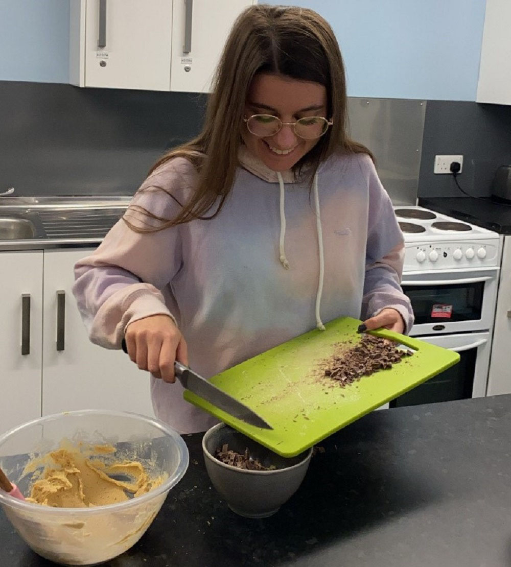 Nyasha's friend putting cut up chocolate into a bowl from a chopping board. 