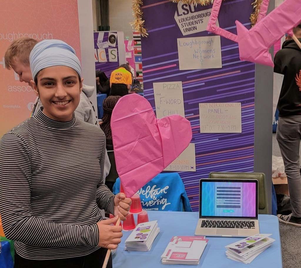 Gugundeep at the Loughborough Women's Network Stall holding a pink paper love heart. 
