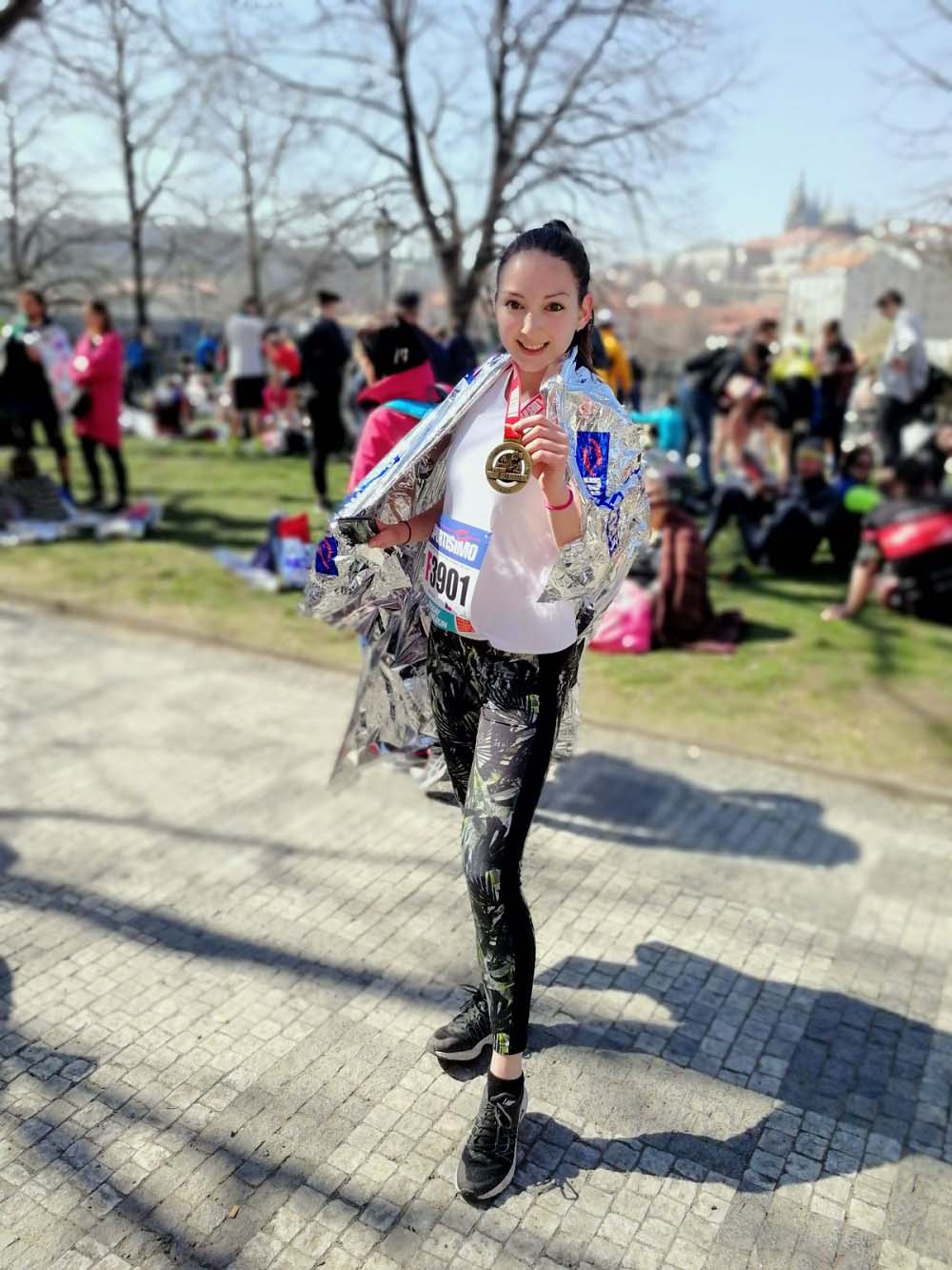 Anastasia after completing the Prague Half Marathon, with a medal around her neck and a foil blanket around her shoulders. 