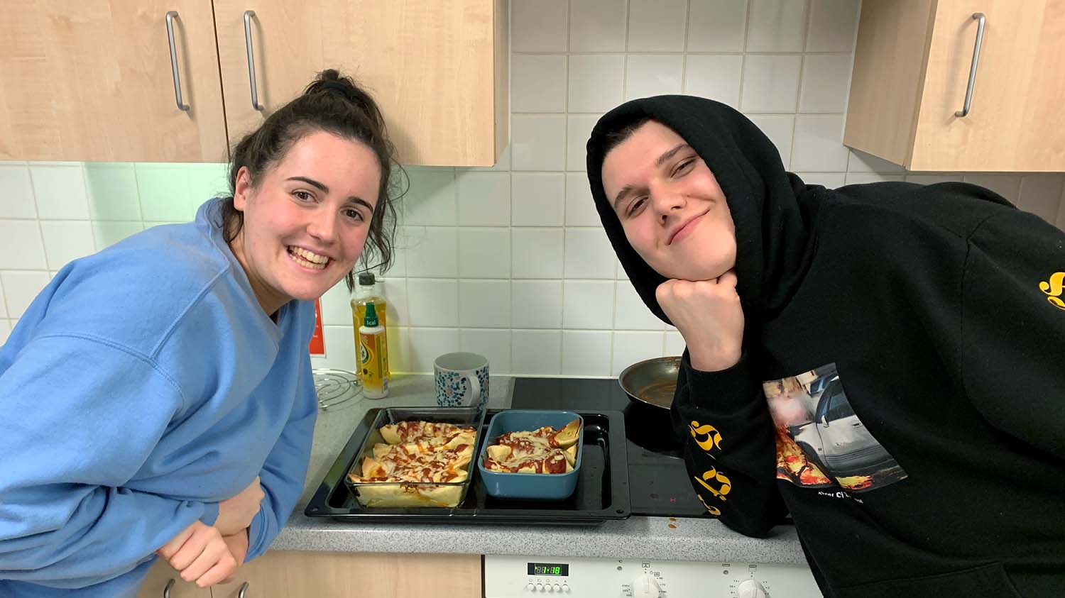 Two students standing next to a meal they have just made. 