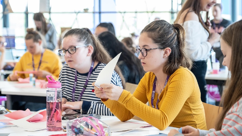 a group of female students sitting at desks working on models