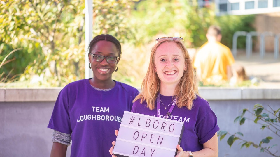 two student helpers one holds a sign reading: Loughborough Open Day