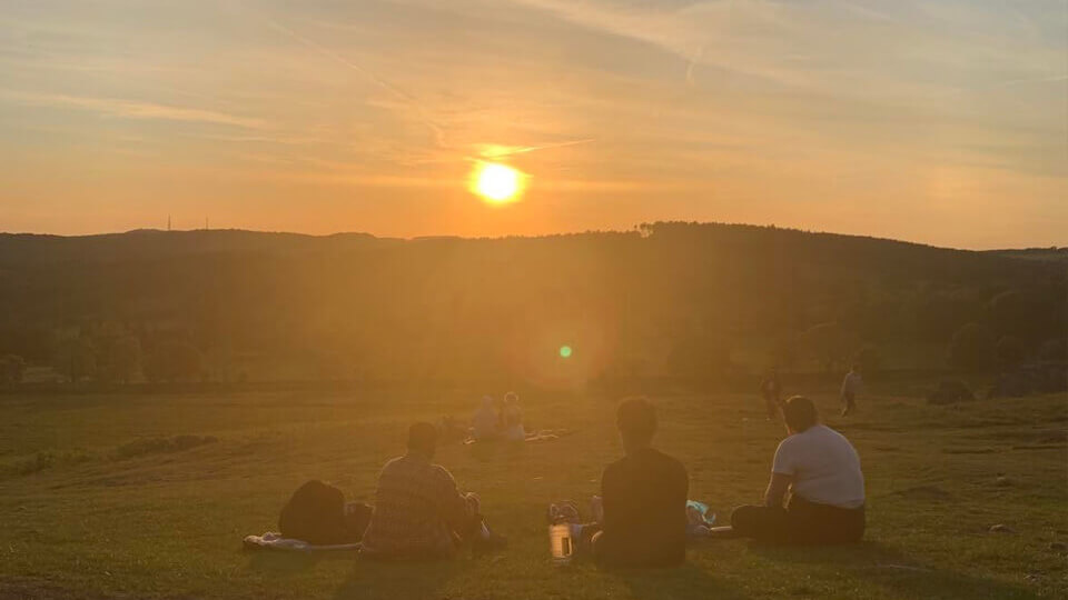 Three students sitting on a hill watching the sun set