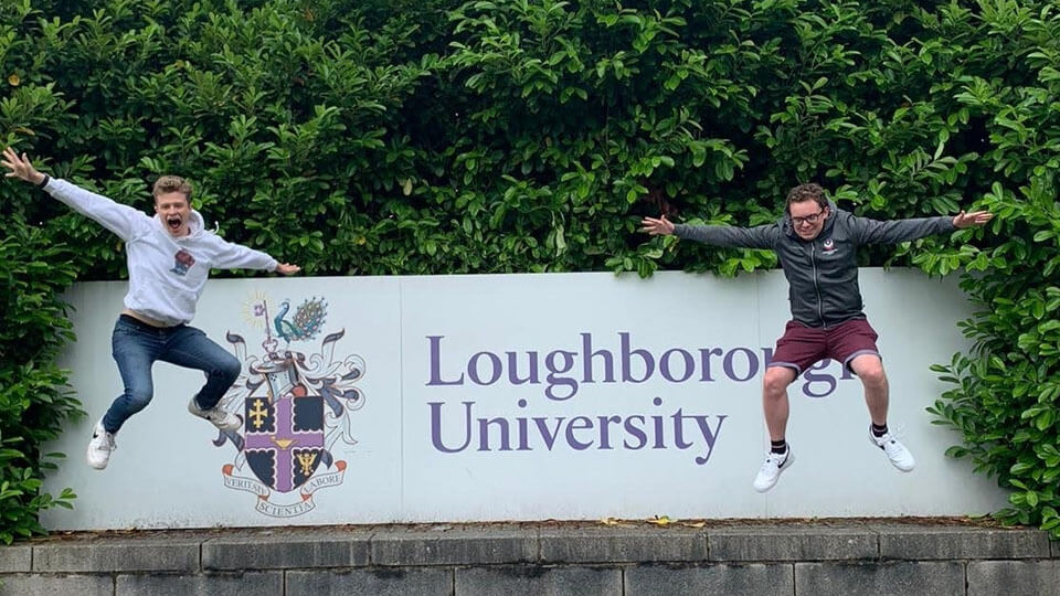 Two students jumping in front of Loughborough University sign