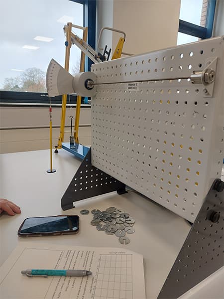 Nikitha's dynamics lab work with white peg board and weights.