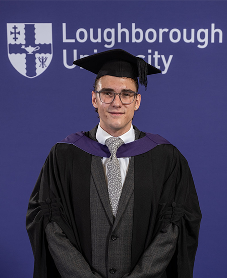 Zachary wearing his graduation gown next to a Loughborough University logo.