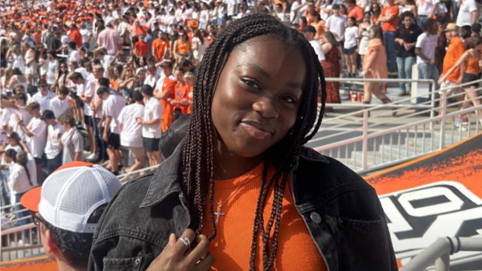 Management BSc student, Gwendoline Datey smiling in a busy Oklahoma State University stadium stand.