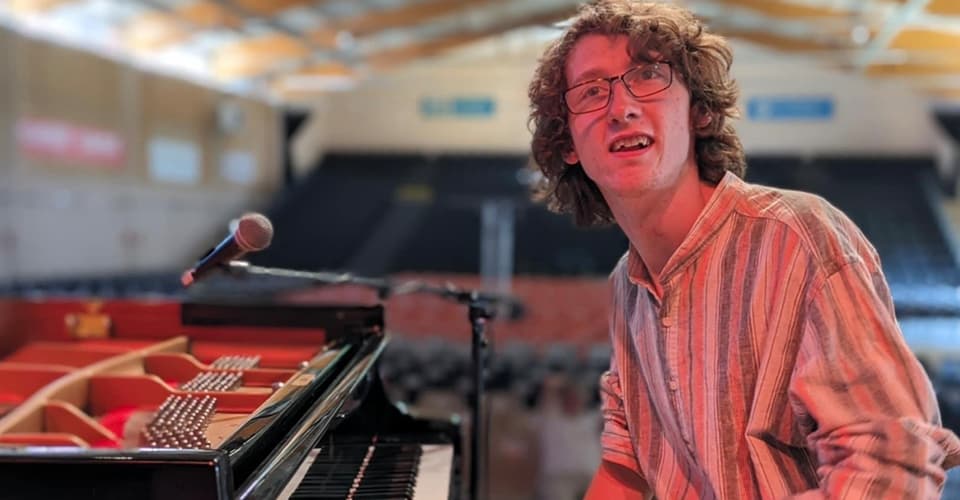 Albert sitting next to a piano on a stage