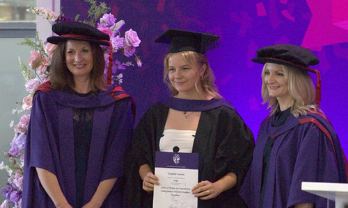 Elizabeth Cummings in her graduation gown being presented with a certificate at her graduation ceremony.