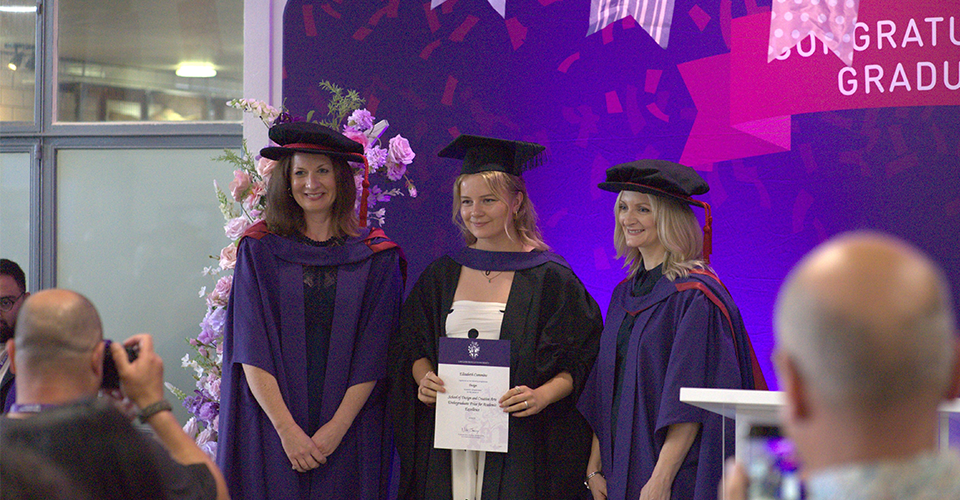 Elizabeth Cummings in her graduation gown being presented with a certificate at her graduation ceremony.