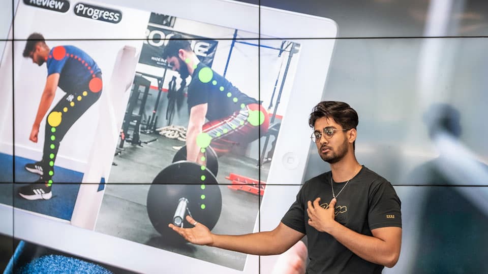 Gaurav Vasnani presenting. On the screen behind are photos of someone weightlifting with a digital analysis of their body.