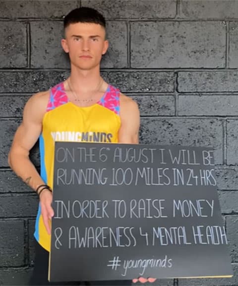 Fin Dearsly in a running top displaying the YoungMinds logo. He is holding a large piece of paper that reads 