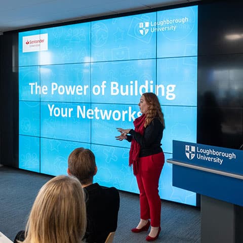 A person delivering a presentation. The screen behind them reads 