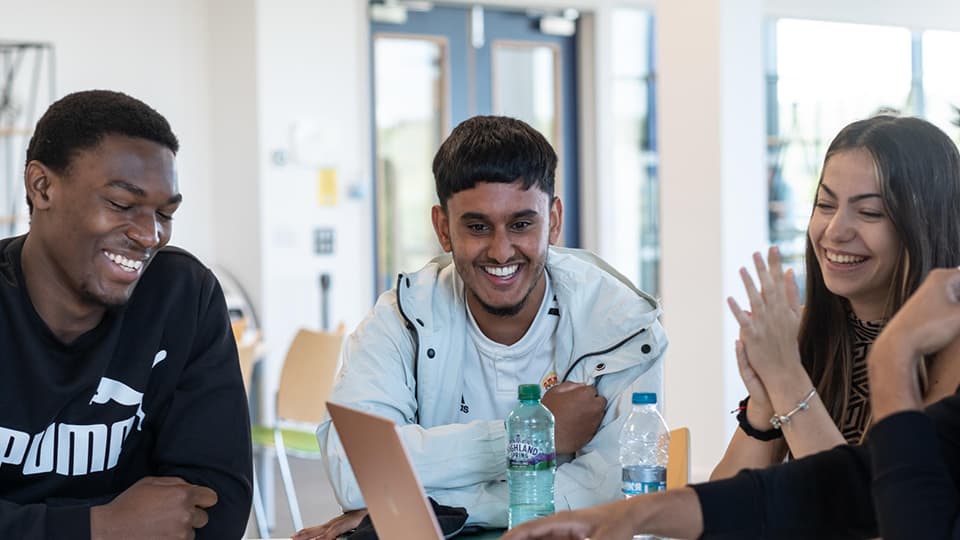 Three students sat together inside chatting and smiling
