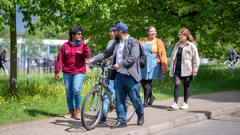 A group of students walking along a pathway on campus with green space in the background