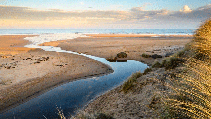 a beach in the UK with a coastal streal and cloudy sky