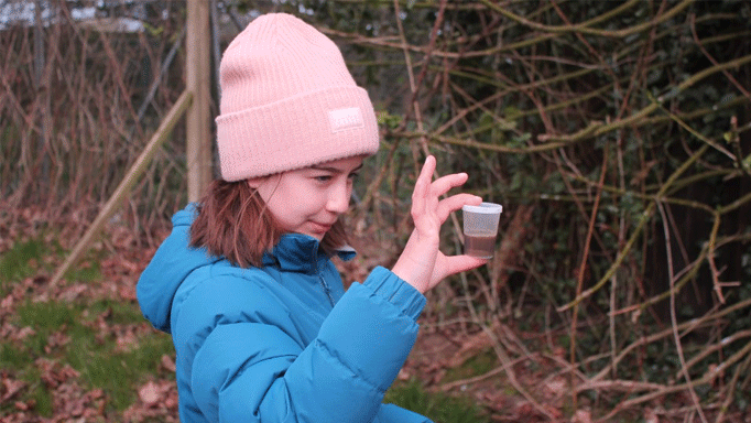 a girl standing outside holding a cup of soil