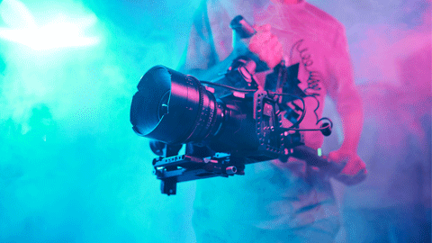 A person operating a camera through blue and purple smoke