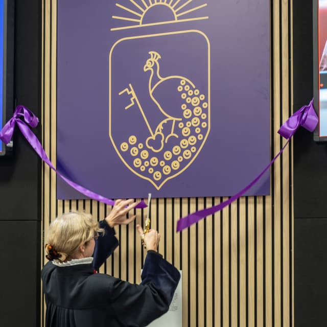 a ribbon in front of the Lboro Law crest in the moot court being cut by a judgeng cut