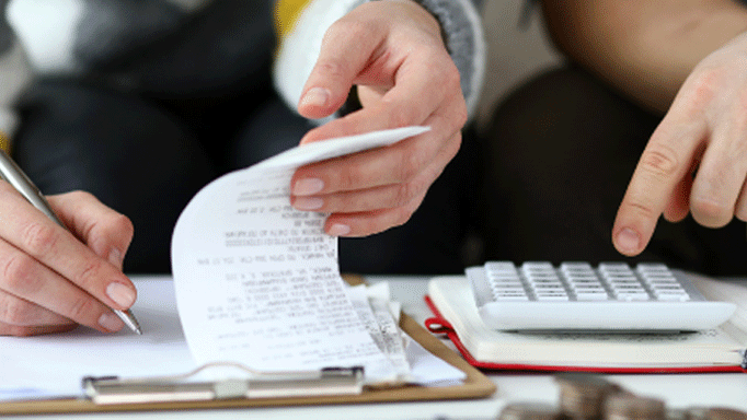 hands of two people using a calculator and looking at a receipt