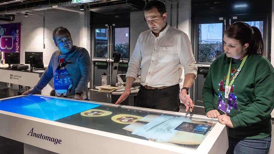 Three people are standing around an interactive table labeled 