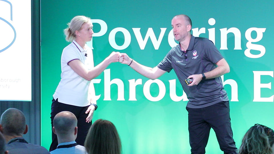Two people standing on a stage giving each other a 'fist bump'