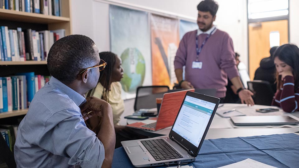 A group of people engage in a collaborative meeting around a table with laptops open