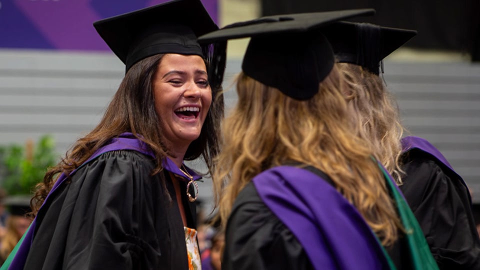 A happy female graduate laughing with fellow graduates in academic gowns and mortarboards.