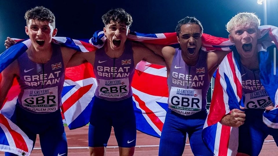 Four British track athletes celebrating draped in the Union Jack flag.