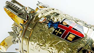 Close-up view of the head of the University mace, with the coat of arms on view, all shiny and bright.