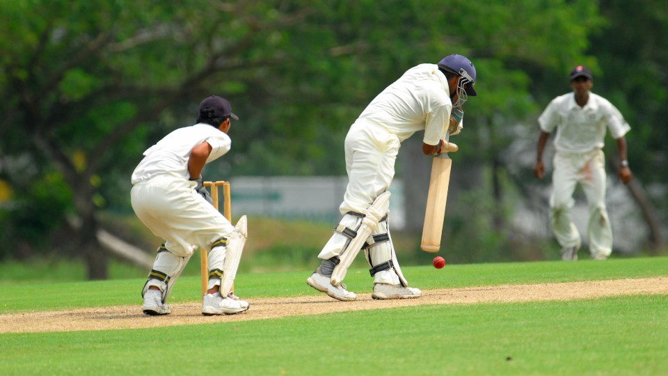 Photo of three men playing cricket on a green 