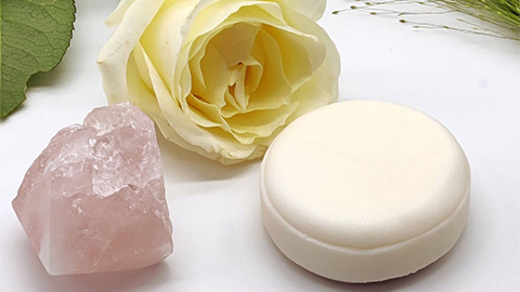 An image of a round block of soap in a cream colour with a rose and a pink crystal