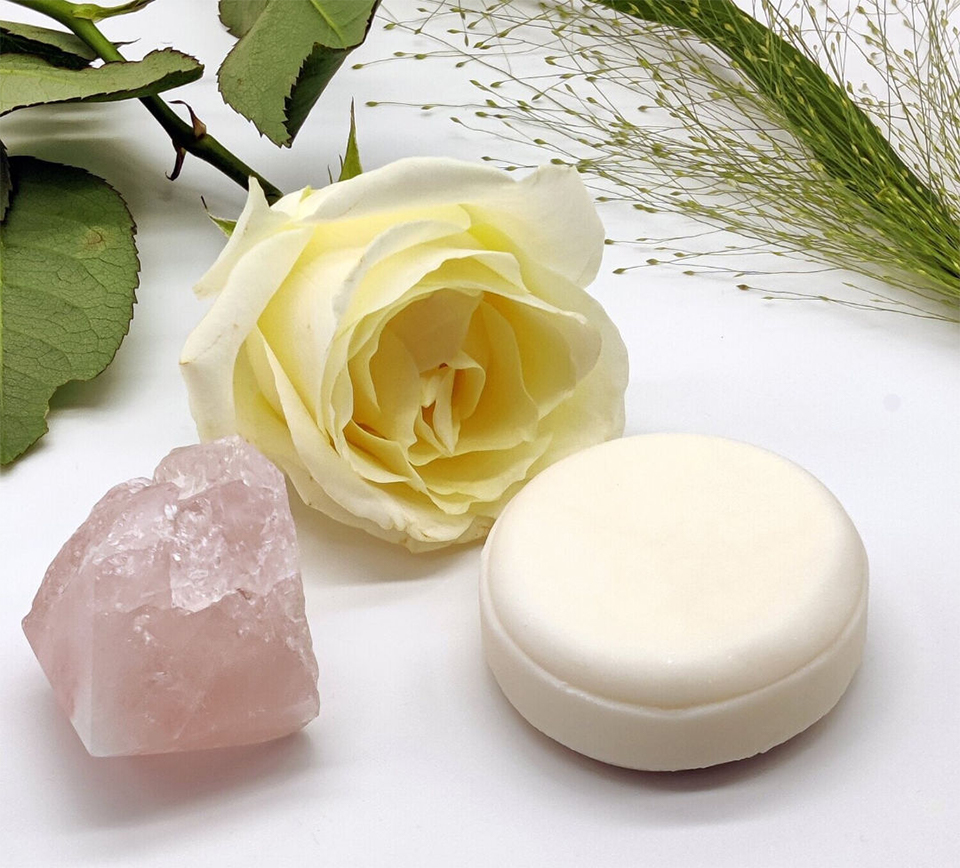 An image of a round block of soap in a cream colour with a rose and a pink crystal