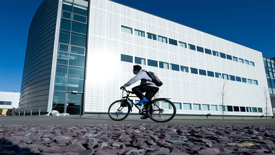 A male student on a bike in front of a building on campus
