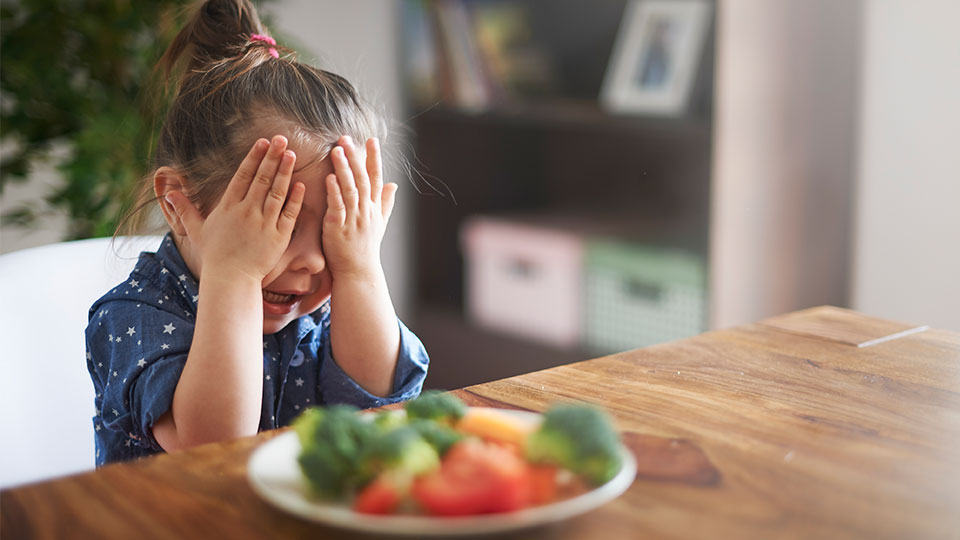 Pictured is a child unhappy about eating vegetables. 